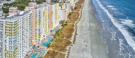 A beachfront hotel with multiple high-rise buildings, a sandy beach, and a clear view of the ocean.