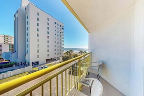 A balcony with a yellow railing overlooking a building and a street. - Bay Watch Resort 0301 (North Myrtle Beach)