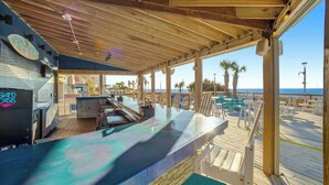 Un área de bar al aire libre con terraza de madera, asientos y vista al océano.