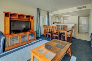 A living room with a television, wooden cabinet, dining table, and chairs. - Bay Watch Resort 0422 (North Myrtle Beach)