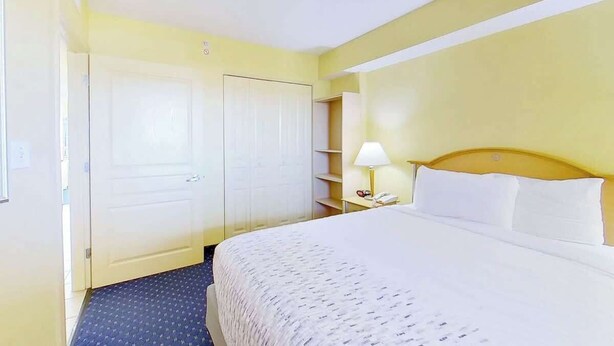 A hotel room with a bed, a nightstand, a lamp, and a wardrobe. - Bay Watch Resort 0505 (North Myrtle Beach)