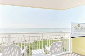 Ein Balkon mit weißen Stühlen mit Blick auf einen Strand. Ein Schild an der Wand zeigt 'Bay Watch Resort – A Conference Center'.