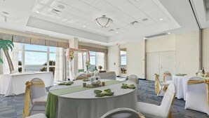 A conference room with round tables, white chairs, and a view of the sea through large windows. - Bay Watch Resort 0505 (North Myrtle Beach)