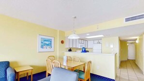 A compact living space with a sofa, dining table, chairs, a kitchenette, and a hallway leading to another room. - Bay Watch Resort 0505 (North Myrtle Beach)