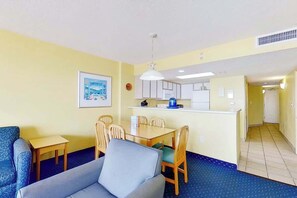 Ein kompakter Wohnraum mit Sofa, Esstisch, Stühlen, einer Küchenzeile und einem Flur, der in einen weiteren Raum führt.