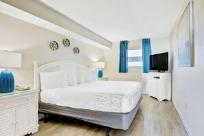 A hotel room with a bed, bedside table, lamp, TV, and a window with curtains. - Bay Watch Resort 0436 (North Myrtle Beach)