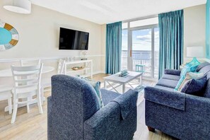 A modern living room with a sofa set, a television, and a dining area with chairs and a table. - Bay Watch Resort 0436 (North Myrtle Beach)