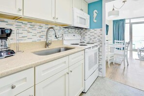 A modern kitchen with white cabinets, a stainless steel sink, a white stove, and a coffee maker. - Bay Watch Resort 0436 (North Myrtle Beach)