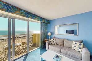 A hotel room with a balcony, a sofa, a coffee table, and a TV. - Bay Watch Resort 0507 (North Myrtle Beach)