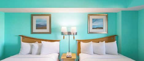 A hotel room with two beds, a nightstand with a lamp, and framed pictures on the walls.