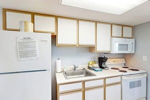 Eine kleine Küche mit Kühlschrank, Mikrowelle, Herd und Spüle.
