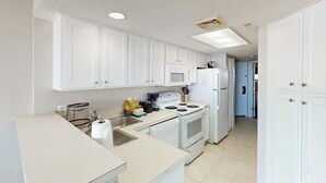 A kitchen with white cabinets, a microwave, stove, and sink. - Bay Watch Resort 0513 (North Myrtle Beach)