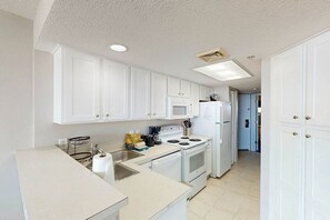 A kitchen with white cabinets, a microwave, stove, and refrigerator. - Bay Watch Resort 0513 (North Myrtle Beach)