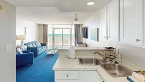 A hotel room with a kitchenette, a sofa set, a dining area, and a view of the ocean. - Bay Watch Resort 0513 (North Myrtle Beach)