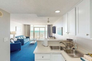 Ein Hotelzimmer mit Küchenzeile, einer Sofagarnitur, einem Essbereich und Blick auf den Ozean.