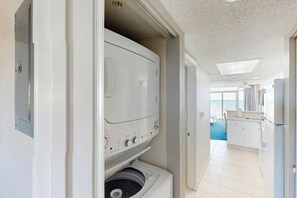 A laundry room with a washer and dryer, a kitchen area with a refrigerator, and a view of the ocean through a window. - Bay Watch Resort 0513 (North Myrtle Beach)