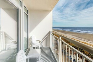 Ein Balkon mit Blick auf den Strand, weißen Stühlen und einem Geländer.