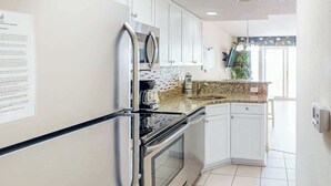 A kitchen with white cabinets, a stainless steel refrigerator, a built-in oven, and a granite countertop. - Bay Watch Resort 0514 (North Myrtle Beach)