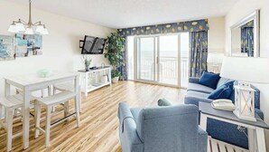 A modern living room with a white table, grey sofa, and a balcony with curtains. - Bay Watch Resort 0514 (North Myrtle Beach)