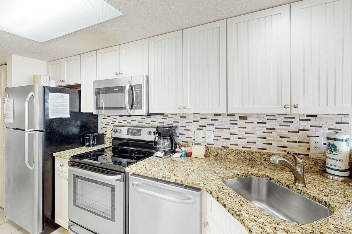 A kitchen with white cabinets, stainless steel appliances, a granite countertop, and a sink.