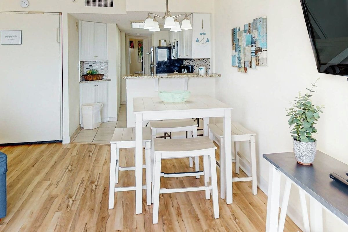 Une cuisine moderne avec des meubles blancs, une table à manger avec des chaises et une plante en pot.