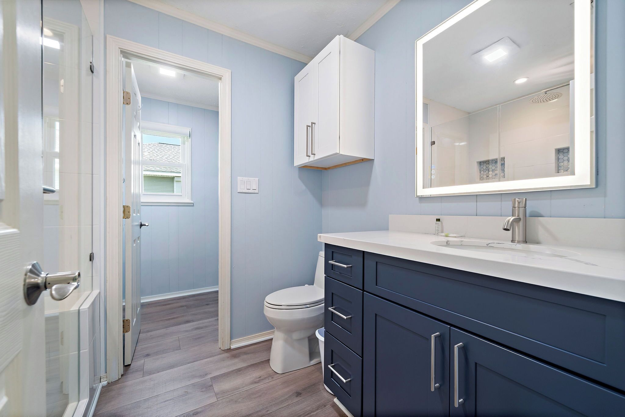 Un baño con inodoro blanco, lavamanos con espejo y armarios azul oscuro.