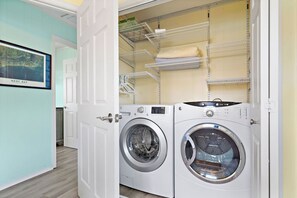 A laundry area with two front-loading washing machines and metal shelving units. - Blue Marlin (Galveston)