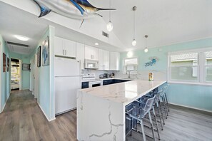 A modern kitchen with white cabinets, a marble island, and a dining area with bar stools. - Blue Marlin (Galveston)