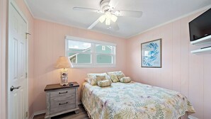 Quarto com cama, mesa de cabeceira, luminária, ventilador de teto, janela e televisão.