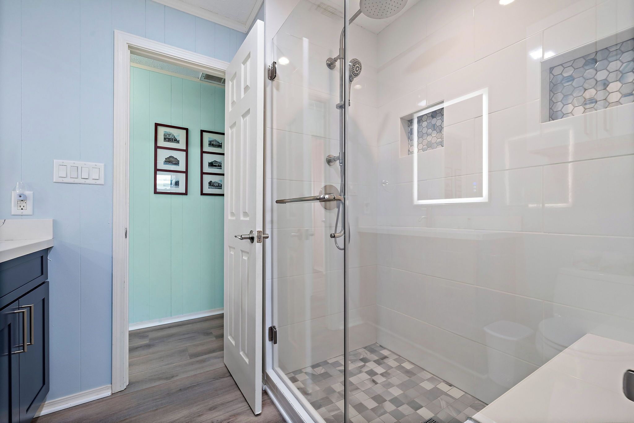 Un bany modern amb una cabina de dutxa de vidre, terra de rajola i una paret de blau clar.
