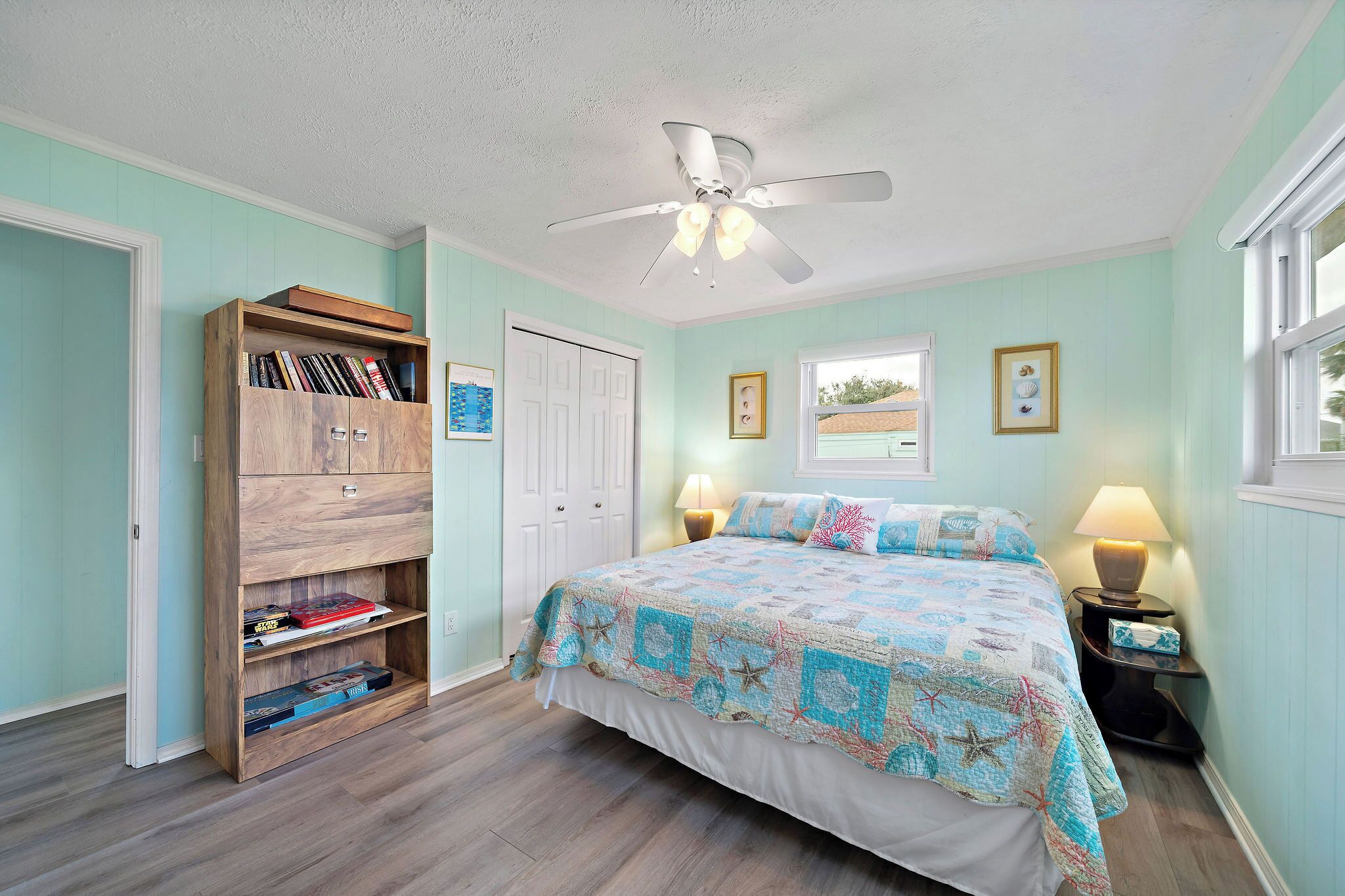 A bedroom with a bed, a wooden bookshelf, a ceiling fan, and a window.