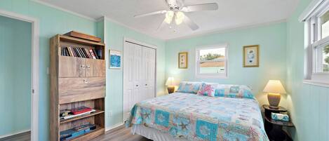A bedroom with a bed, a wooden bookshelf, a ceiling fan, and a window.