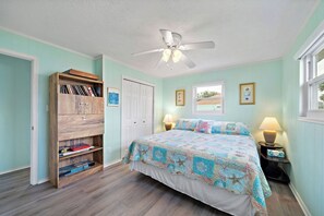 A bedroom with a bed, a wooden bookshelf, a ceiling fan, and a window. - Blue Marlin (Galveston)