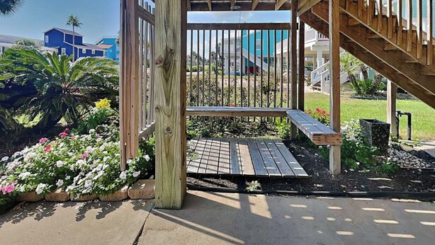 Um deck de madeira com um banco, rodeado por um jardim com diversas plantas e flores.