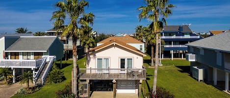 A single-story house with a front porch, a garage, and a small backyard with palm trees and a lawn.
