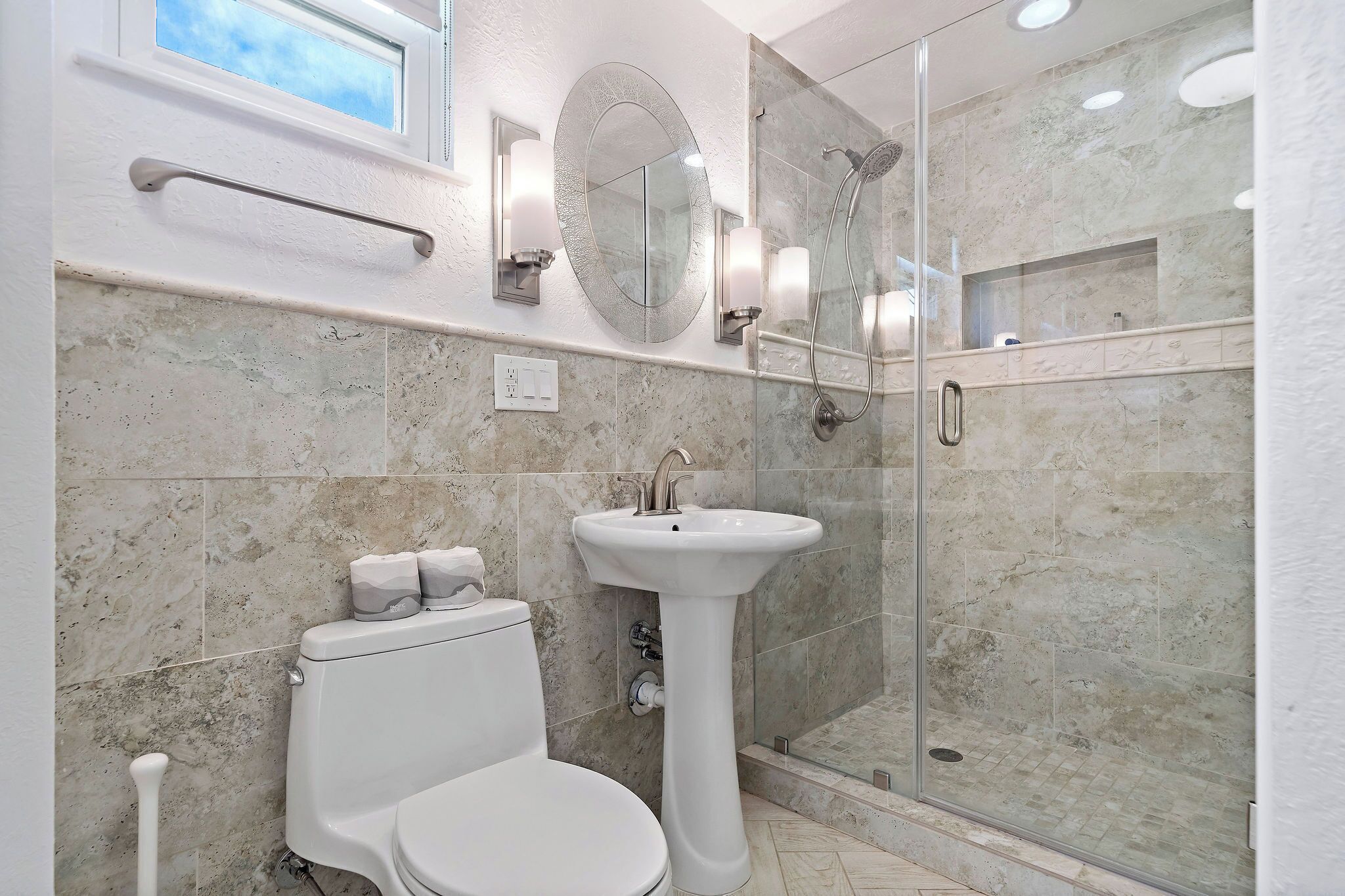 A modern bathroom with a toilet, pedestal sink, and glass-enclosed shower.