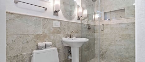 A modern bathroom with a toilet, pedestal sink, and glass-enclosed shower.