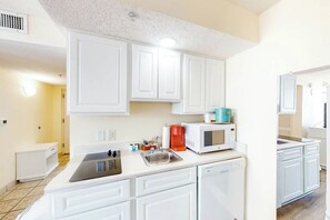 A modern kitchen with white cabinetry, a built-in microwave, and a coffee maker. - Bay Watch Resort 0531 (North Myrtle Beach)