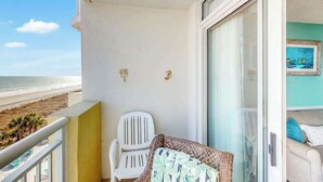 Ein Balkon mit einem weißen Stuhl, einem Korbsessel und Blick auf den Strand.