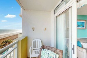 Ein Balkon mit einem weißen Stuhl, einem Korbsessel und Blick auf den Strand.