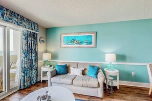 Ein Zimmer mit einer türkisfarbenen Wand, einem beigen Sofa mit blauen und weißen Kissen, einem weißen Couchtisch und einem gerahmten Gemälde über dem Sofa.