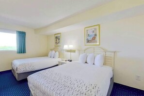 A hotel room with two beds, a window with curtains, a nightstand with a lamp, and two framed pictures on the wall. - Bay Watch Resort 0613 (North Myrtle Beach)