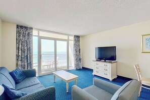 A hotel room with a balcony, a television on a dresser, and two sofas. - Bay Watch Resort 0613 Oceanfront (North Myrtle Beach)