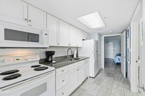 A modern kitchen with white cabinetry, a built-in microwave, a stove, and a refrigerator. - Bay Watch Resort 0603 (North Myrtle Beach)