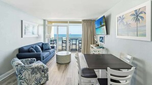 Une pièce comprenant un canapé, une table à manger, des chaises, un téléviseur et un balcon avec vue sur la mer.