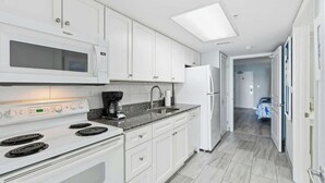 Une cuisine moderne avec des meubles blancs, un four à micro-ondes encastré, une cuisinière et un réfrigérateur.