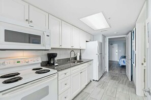 A modern kitchen with white cabinetry, a built-in microwave, a stove, and a refrigerator. - Bay Watch Resort 0603 (North Myrtle Beach)