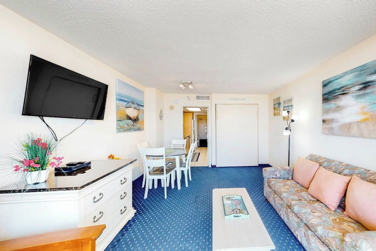 Un espace de vie compact comprenant un téléviseur à écran plat fixé au mur, un coin repas avec une table et des chaises, un canapé et une petite table basse.