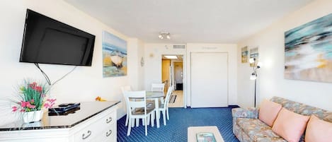 Un espace de vie compact comprenant un téléviseur à écran plat fixé au mur, un coin repas avec une table et des chaises, un canapé et une petite table basse.