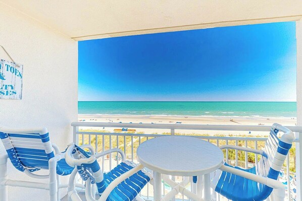 A balcony with a view of the beach, a table, and two chairs. - Bay Watch Resort 0534 (North Myrtle Beach)